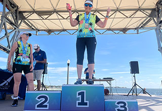 A woman in an athletic suit stands on the winner’s podium after accepting an award.